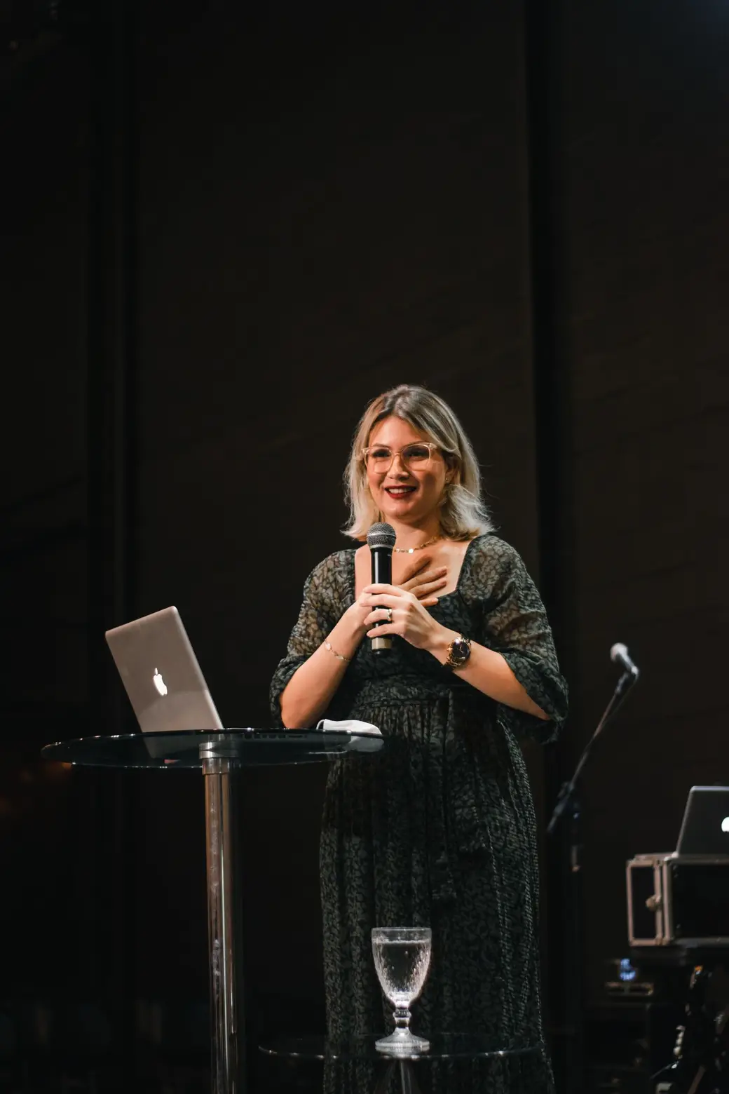 A woman speaking on stage with a microphone, smiling at her audience