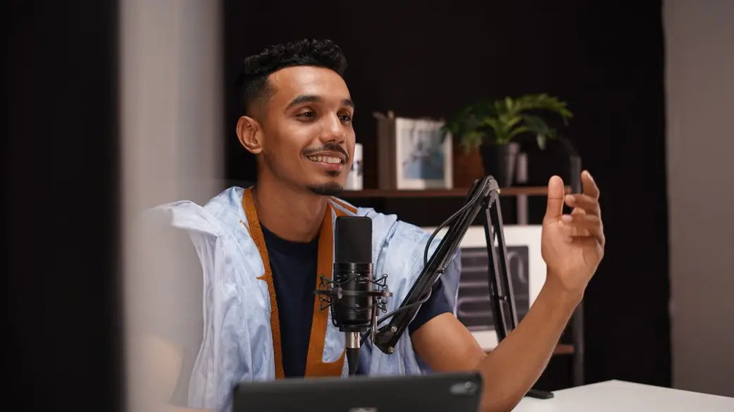 A smiling man recording a podcast in a warm home studio