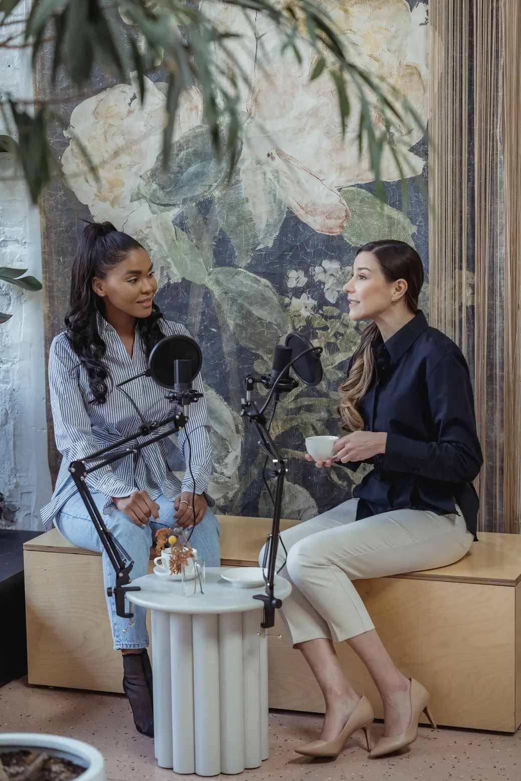 Two women in conversation at a podcast recording, microphones between them