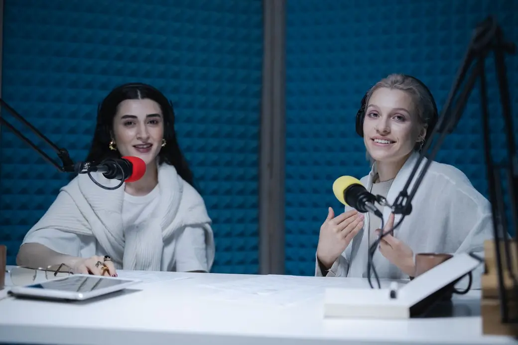 Two women recording a podcast together in a studio with blue sound panels