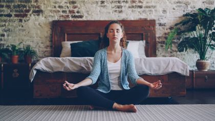 A woman meditating with her eyes closed in a sunlit bedroom