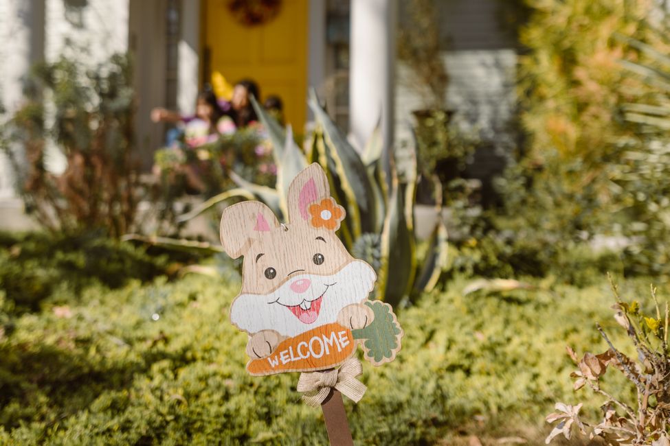 A cheerful Easter bunny welcome sign in a sunlit garden setting.