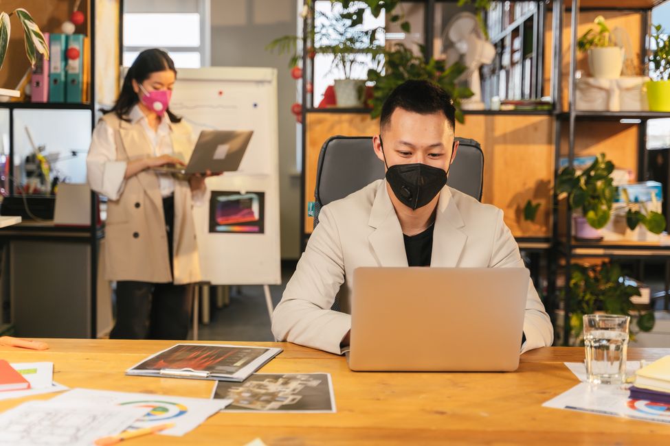 Professional team collaborating in modern office with safety measures observed, including masks.
